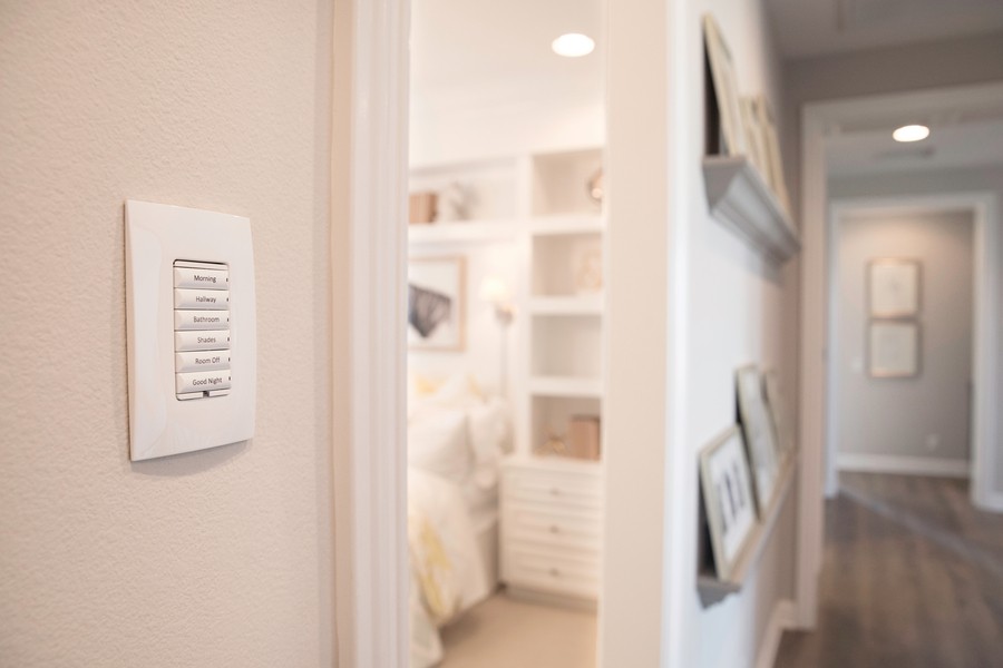 A modern smart home keypad on the wall, with options for 'Morning', 'Hallway', 'Bathroom', 'Shades', 'Room Off', and 'Good Night' for easy home automation