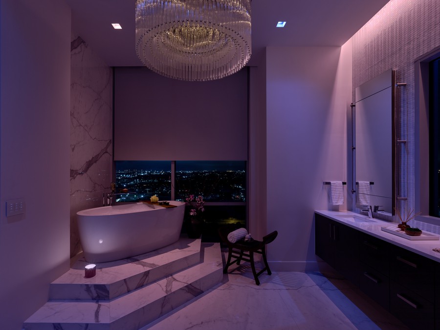 A master bathroom with a soaking tub and chandelier illuminated in violet by Lutron’s Ketra lighting.