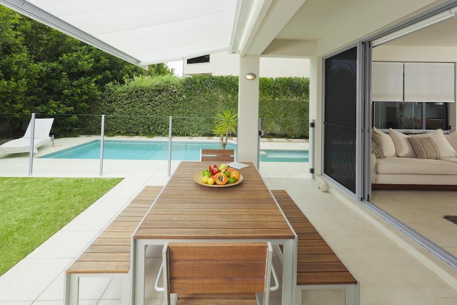 An outdoor patio with a pool in the background and a picnic-style table in the foreground.