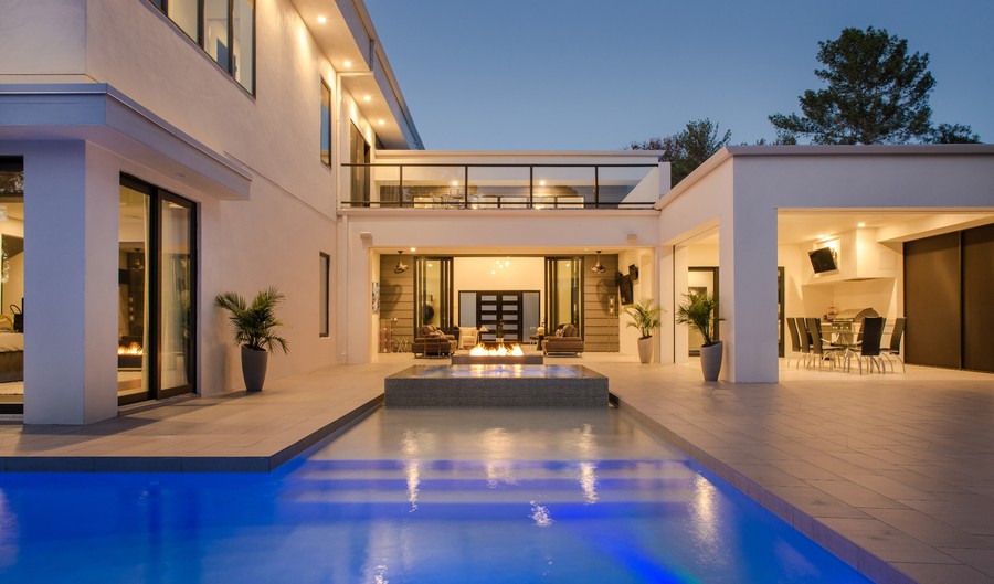  A well-lit home with a pool and fireplace after dark. The pool is illuminated with bright blue light.