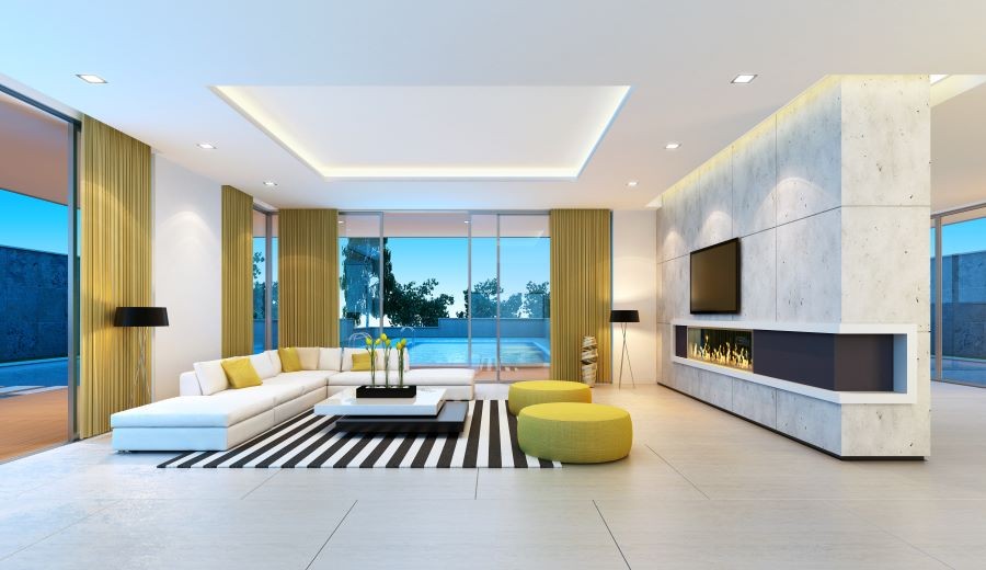A modern living room with a flat-screen TV above a lit fireplace and open class doors revealing a pool.