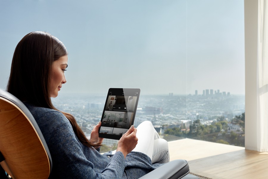 A woman sitting in a chair overlooking the city. She’s holding an iPad displaying the Savant home automation app.